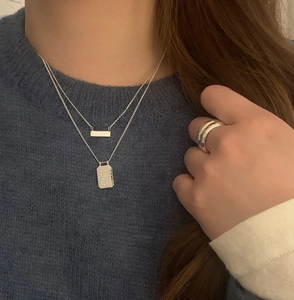 Close-up of double-layer silver 925 necklaces and wide ring worn on blue knitwear