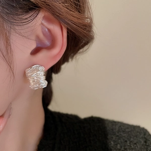 Detail of silver metallic crumpled texture earring worn by a model in soft lighting