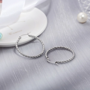 Detailed macro shot of silver twist-textured hoop earrings on an elegant white ribbon