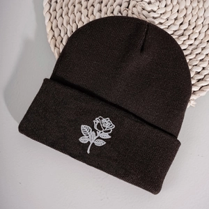 Close-up of white rose embroidery on a dark knit beanie with soft ribbed texture