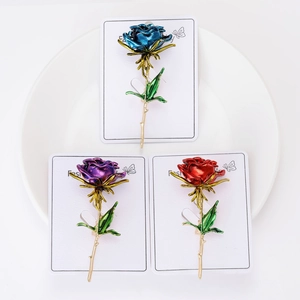 Three-piece rose brooch set in blue purple and red enamel on a white ceramic plate