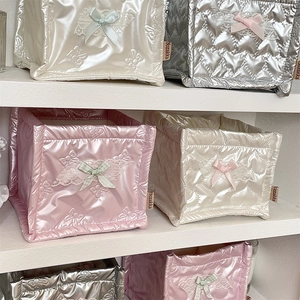 Detail of quilted satin storage boxes with lace trim and bows on a white shelf