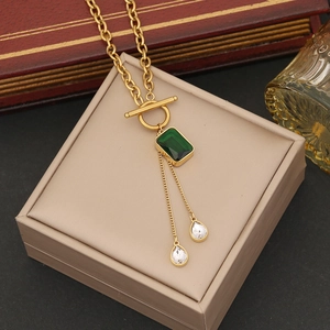 Gold necklace with green square pendant and water drop charms on beige display