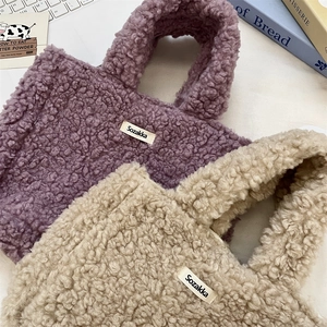 Detail of plush lamb wool handbags in purple and beige with woven label on soft surface
