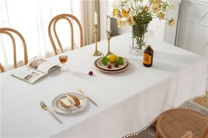 Close-up of a white cotton rectangular tablecloth featuring decorative pompom fringe edges