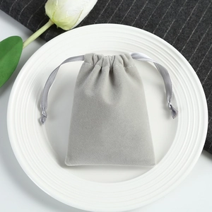 Close-up of a grey velvet drawstring jewelry pouch on a white plate with tulips