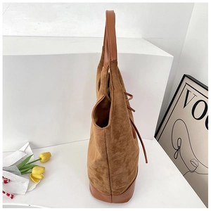 Side view of brown faux suede bucket tote bag with leather straps on minimalist display