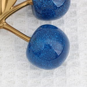 Makro-Detail von blauem Glitzer-Kirsch-Anhänger mit goldenem Metallstiel auf Stoff