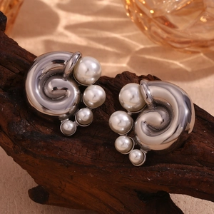 Macro detail of silver spiral wave earrings with white pearls on a vintage wooden base