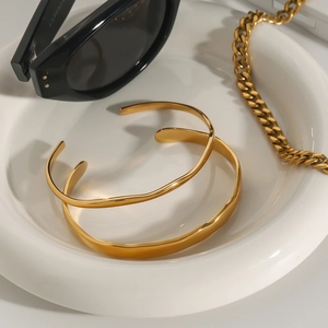 Polished gold wavy open bangles set on white ceramic tray with fashion accessories