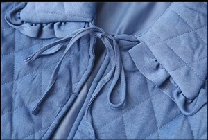 Detail of blue quilted jacket with diamond patterns, ruffle collar and tie-up front closure