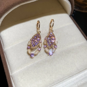 Macro detail of vintage gold drop earrings with purple gemstones and oval opal accents