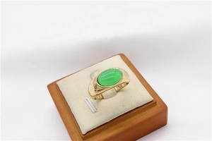 Detailed top view of a gold wide band ring set with a large oval green gemstone