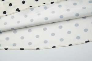 Dettaglio del tessuto bianco a pois neri con bordo in pizzo delicato e texture morbida