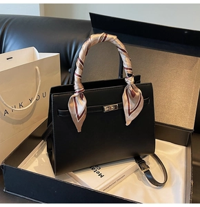 Close-up of black leather handbag with gold lock, silk scarf handle, and gift packaging