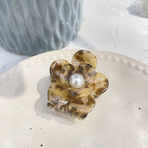 Detail of a brown tortoiseshell floral hair claw clip featuring a pearl center on a ceramic plate