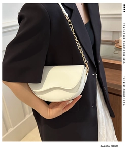 Gros plan d'un sac selle demi-lune blanc avec chaîne dorée porté par un mannequin mode