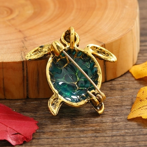 Vintage sea turtle brooch with green enamel and gold plating on an autumnal wooden background