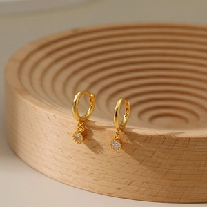 Elegant gold-plated hoop earrings featuring a round zircon drop on a wooden tray