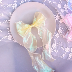 Close-up of a pale yellow organza bow hair clip with iridescent sheen on a lace plate