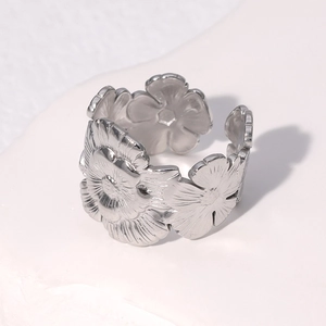 Silver flower-shaped open ring in stainless steel on a white textured background