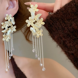 Close-up of golden butterfly flower earrings with long silver tassels and crystal beads