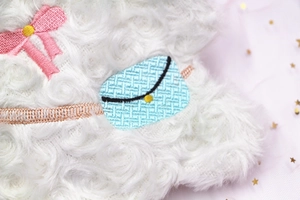 Détail du tissu peluche blanc avec broderies de nœud rose et petit sac bleu ciel