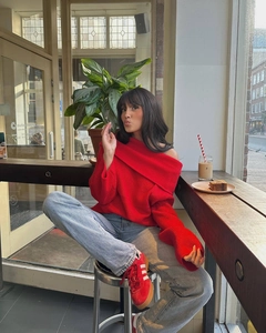 Détail d'un pull en maille rouge à épaules dénudées avec un jean bleu clair et des baskets