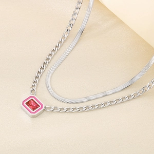 Detail of layered silver Cuban and snake chains with a red crystal and pink enamel pendant