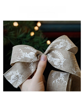 Macro detail of natural burlap Christmas ribbon with white reindeer and floral print decor