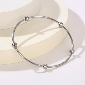 Detail of silver titanium steel bangle with five metal beads on white display stand