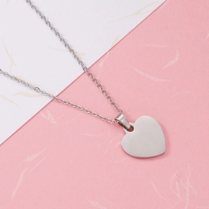 Close-up of polished silver heart pendant on O-chain necklace over textured background