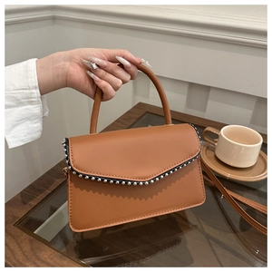 Close-up of brown PU leather handbag with silver stud trim in an elegant cafe setting