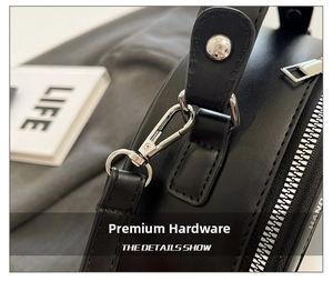 Close-up of polished silver-tone metal lobster clasp and zipper on a black leather handbag