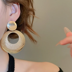 Gros plan d'une boucle d'oreille disque doré évidé avec texture radiale sur le mannequin