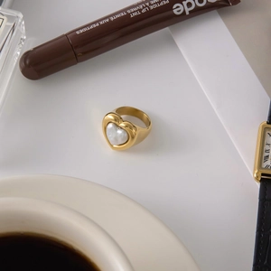 Detail of a gold heart ring with pearl inlay set against a cozy coffee lifestyle background