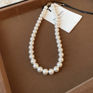 Detailed view of glossy white pearl necklace with branding tag on velvet display tray