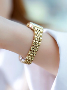 Close-up of a polished gold-tone link bracelet watch worn on a wrist in elegant lighting