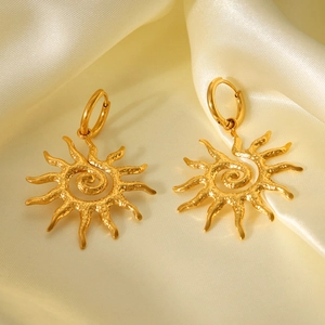 Detailed close-up of 18K gold-plated sun-shaped earrings on elegant champagne silk fabric