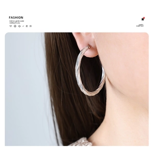 Close-up of large twisted silver hoop earrings worn by a model for a fashion look