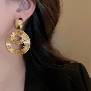 Macro view of gold multilayer geometric spiral earrings worn on model's ear