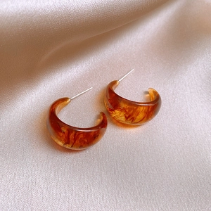 Detailed view of C-shaped resin hoop earrings with amber tortoiseshell texture on silk