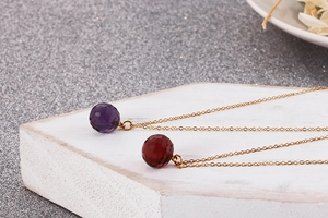 Detail of dual faceted crystal pendants in purple and garnet red on fine gold chains