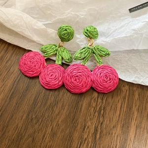 Close-up of woven pink cherry earrings with green leaves on a textured paper surface
