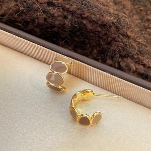 Close-up of golden C-shaped hoop earrings with brown enamel on beige jewelry padding