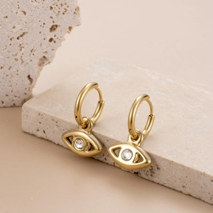 Golden double hoop earrings with evil eye charm and clear zircon on a beige rock