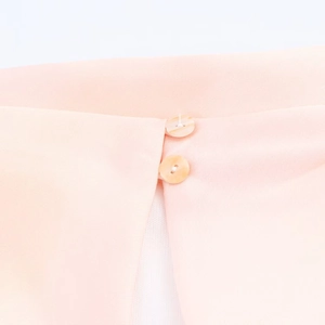 Detalle macro de un vestido de satén rosa claro con dos botones redondos nacarados