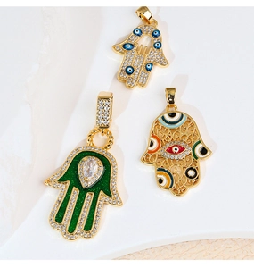 Dettaglio di tre ciondoli Hamsa dorati con smalto colorato e decorazioni in zirconi
