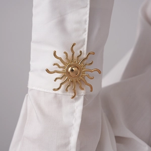 Macro view of a golden sunburst brooch set on a white shirt cuff with rich metal textures