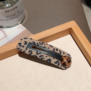 Close-up of leopard print fabric hair clip with a matching bead detail on a rustic background